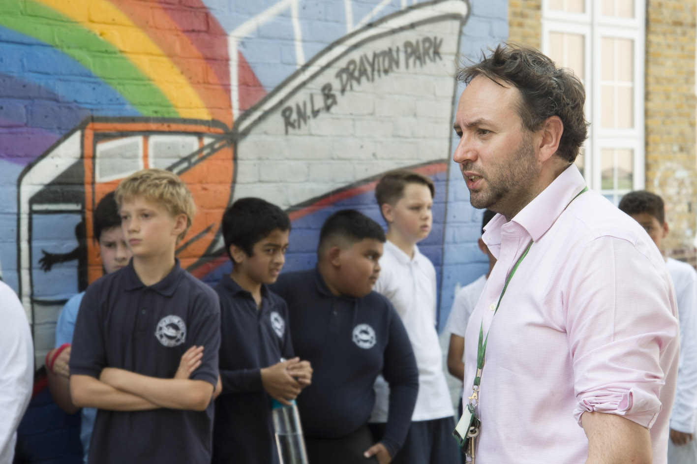 A teacher in the playground with pupils queuing 