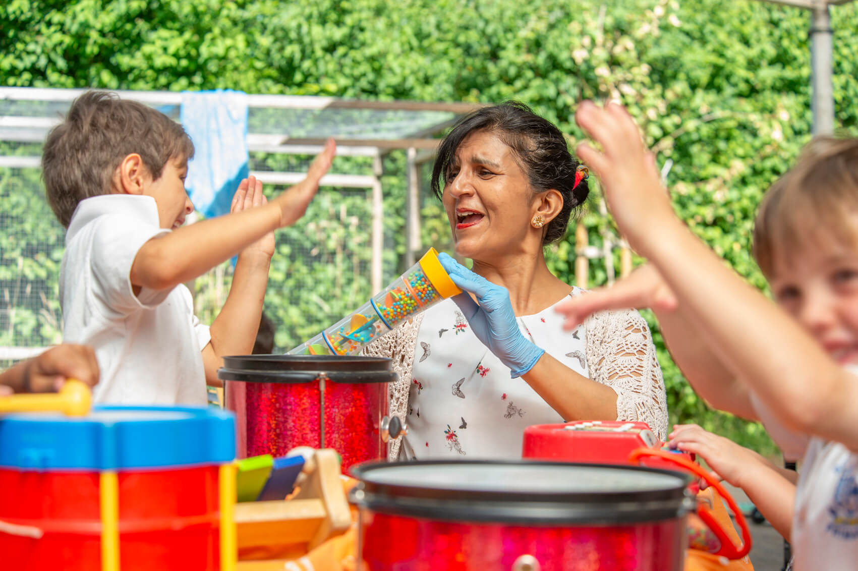 A teaching assistant laughing with musical instruments in an outdoor play area