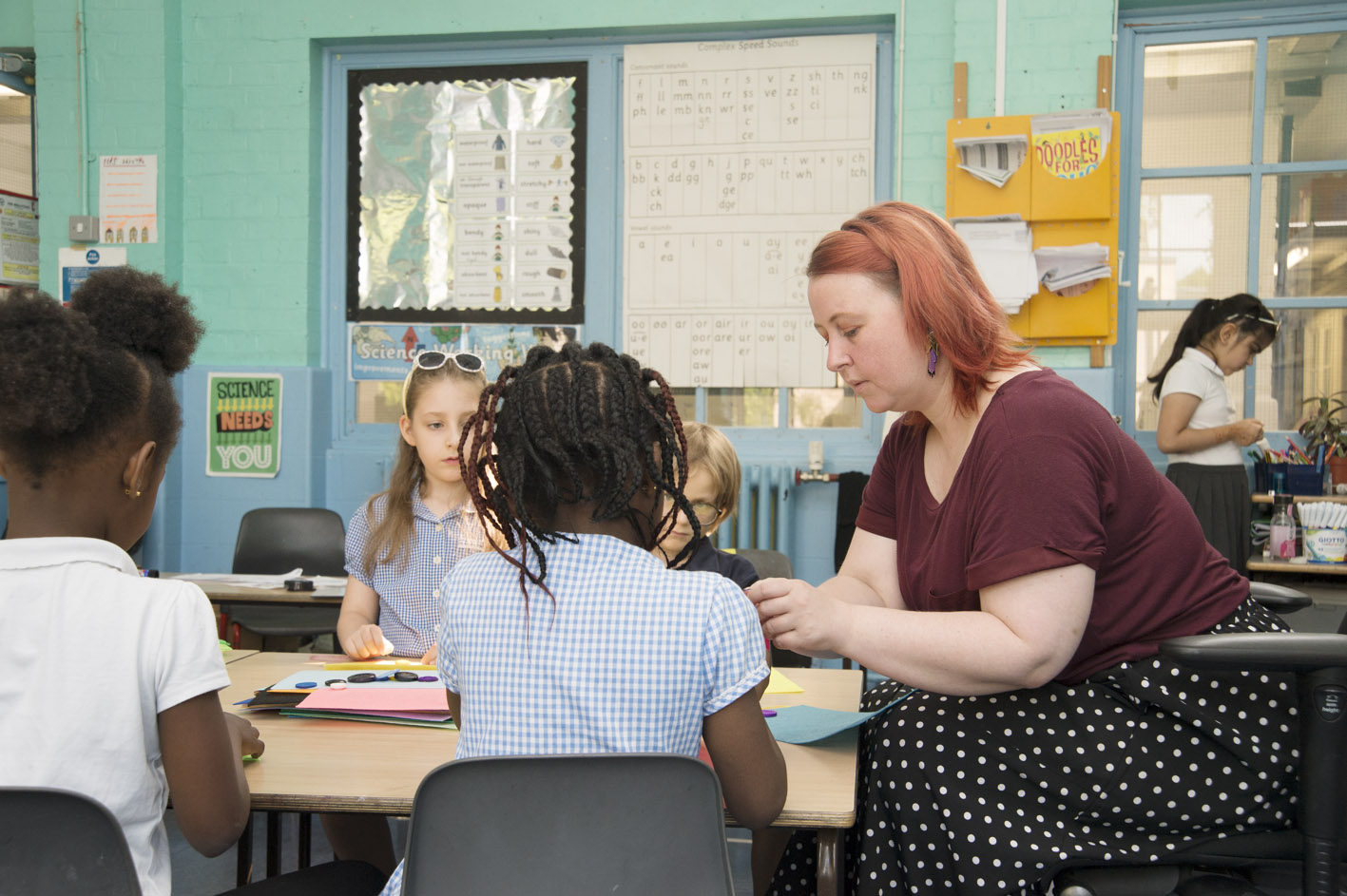 A teacher sitting at with pupils in a classroom