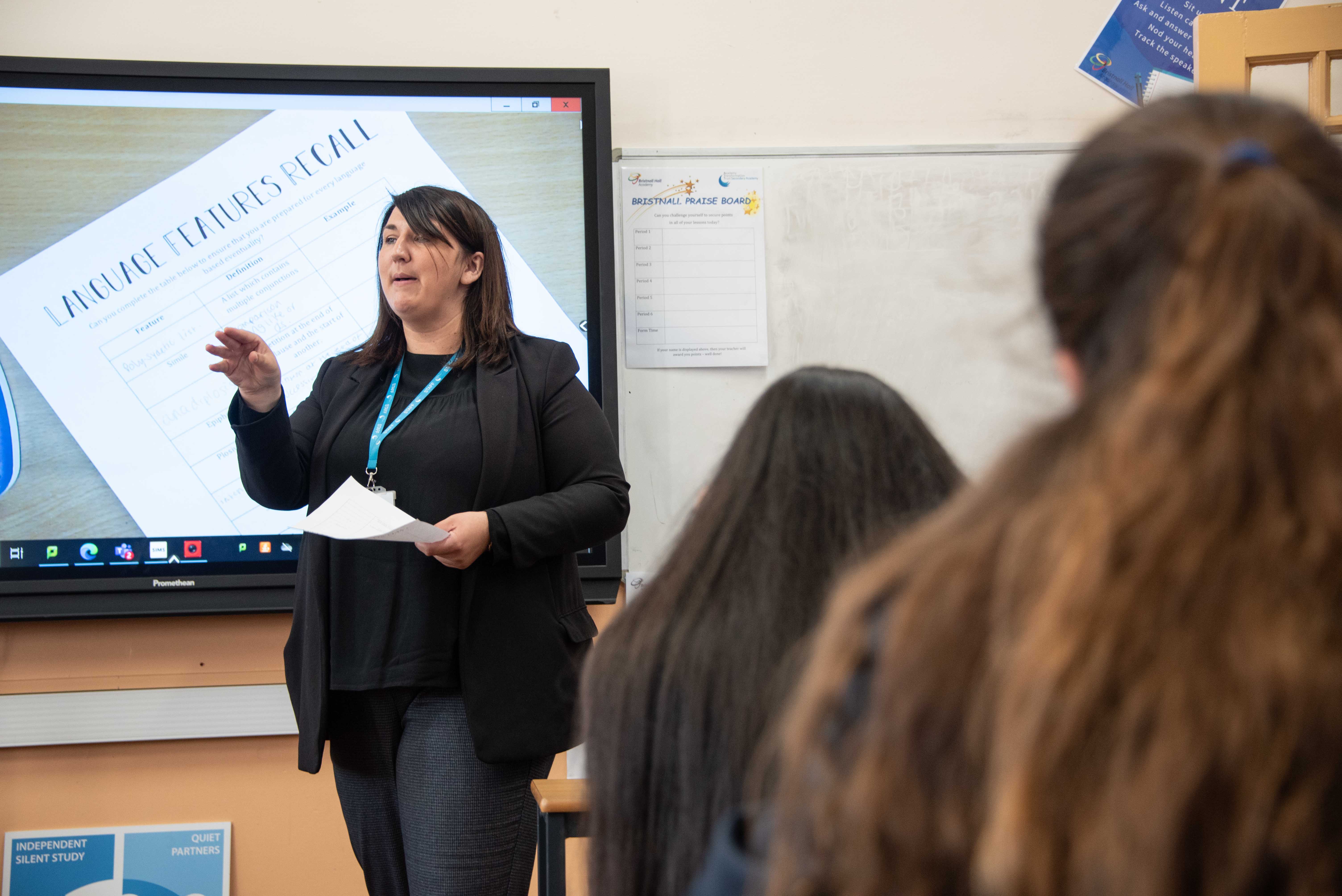 A teacher standing at the front of a classroom talking to students