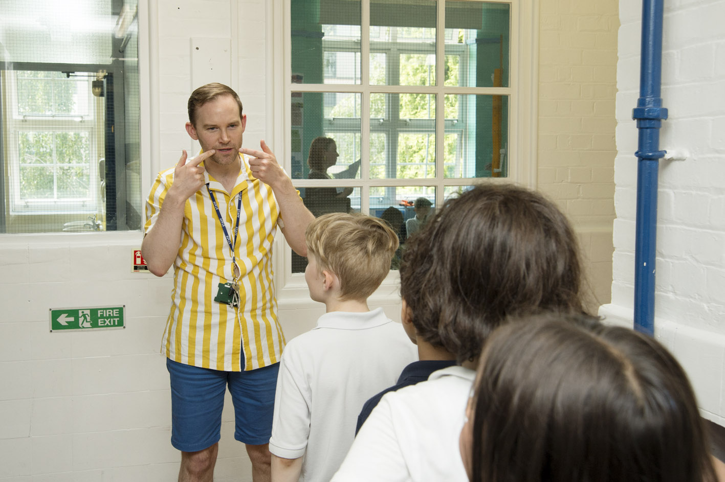 A teacher in a school hallway with pupil queuing 