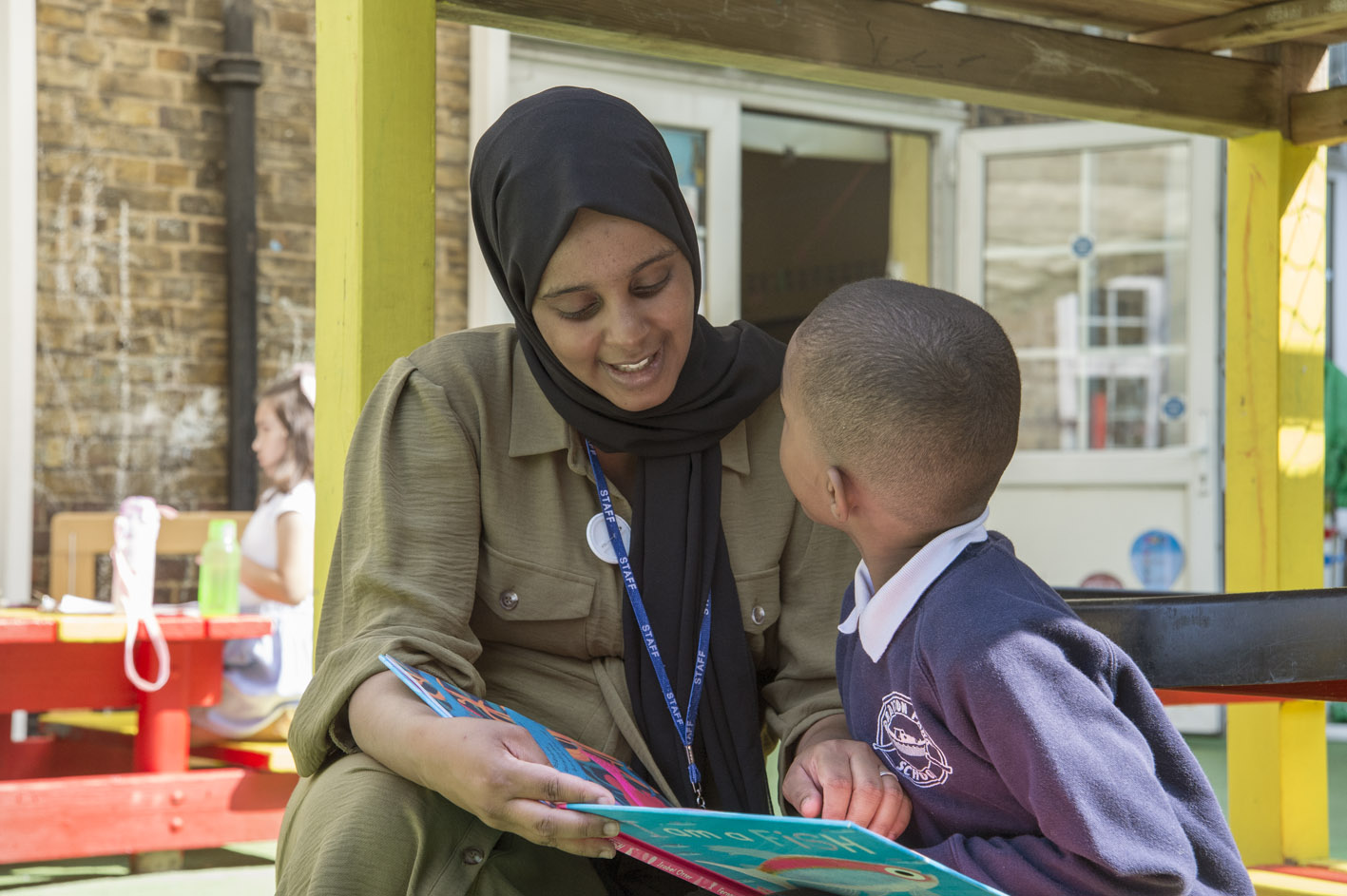 A smiling teaching assistant helping a pupil 