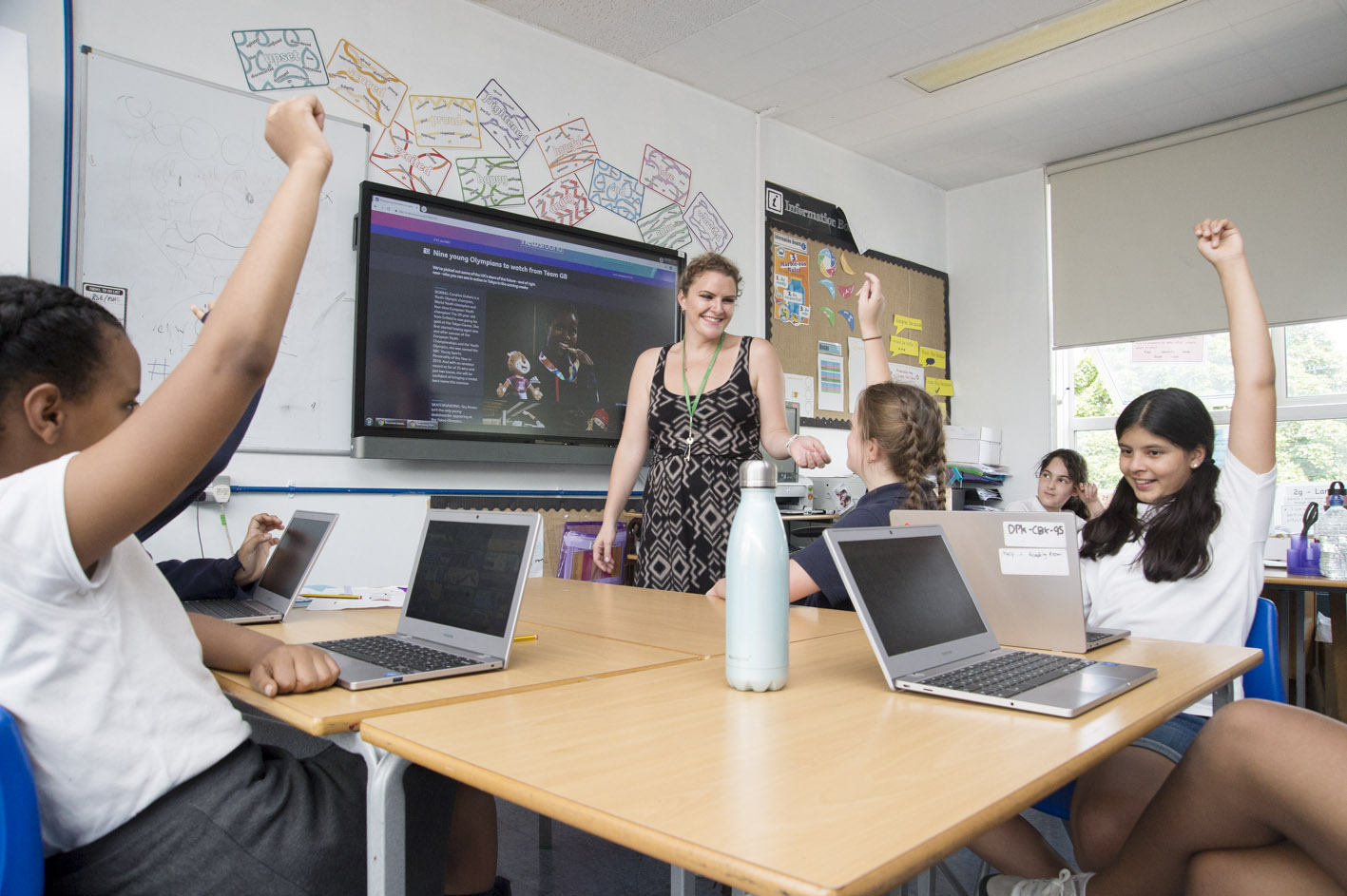 A teacher in a classroom with pupils with their hands up