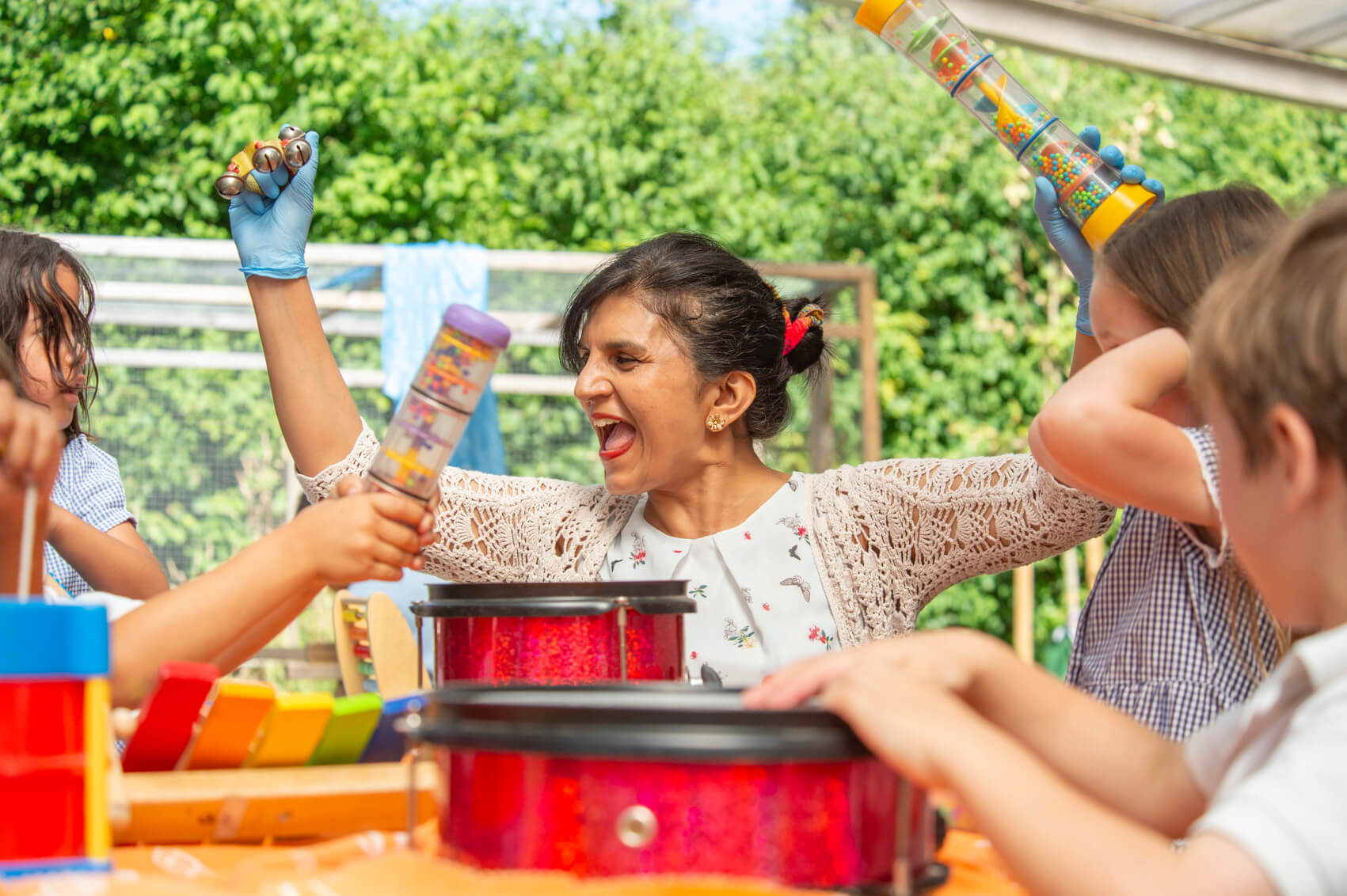 A teaching assistant laughing with musical instruments in an outdoor play area