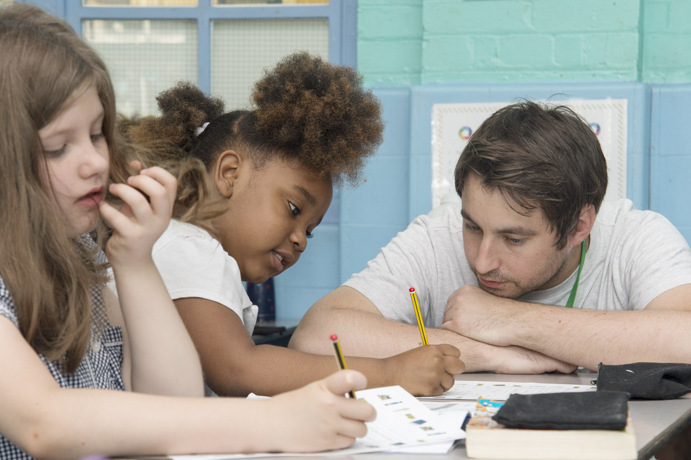 A teacher helping two pupils sitting at a desk
