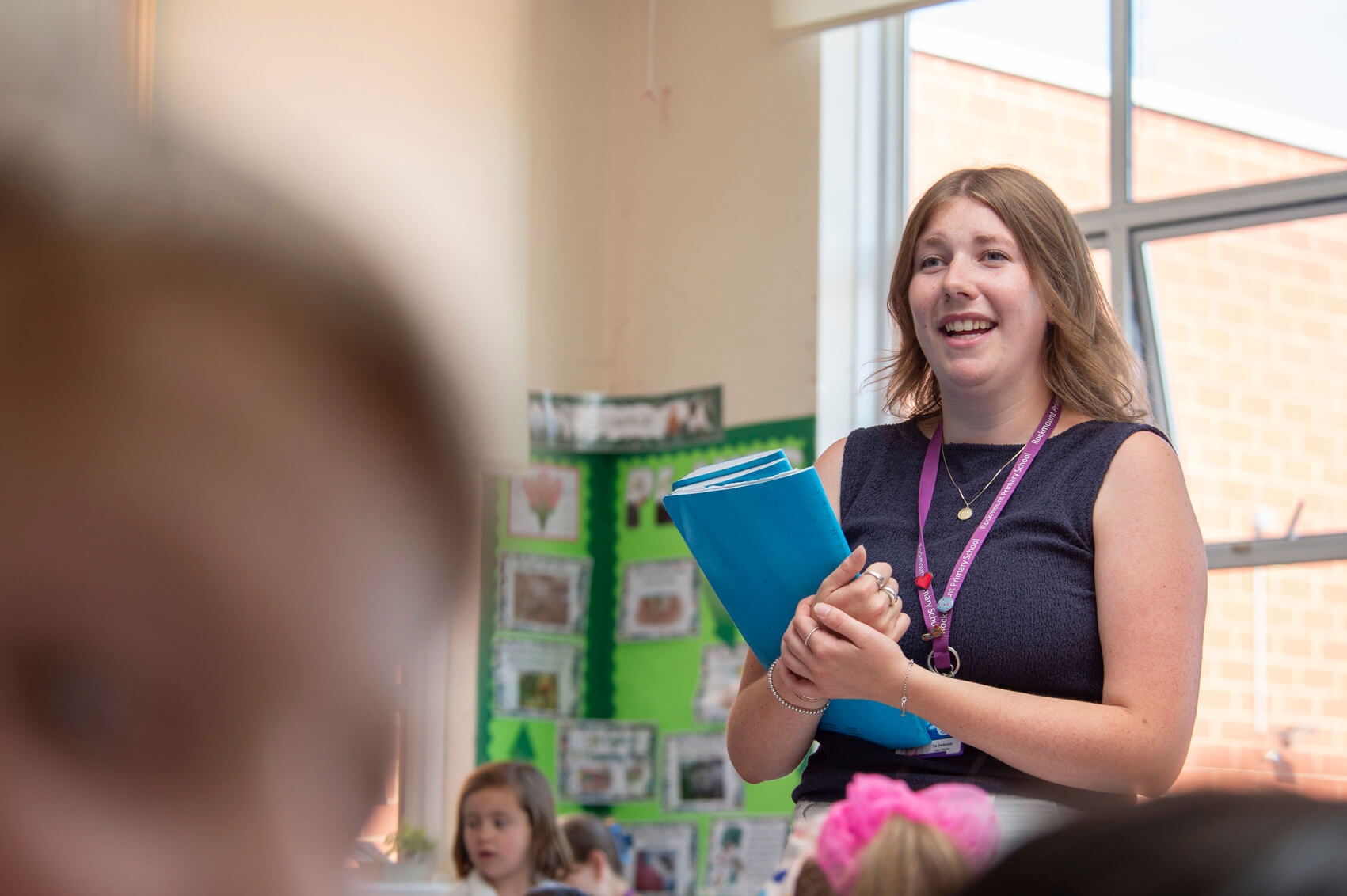 A teacher smiling at the front of a classroom 
